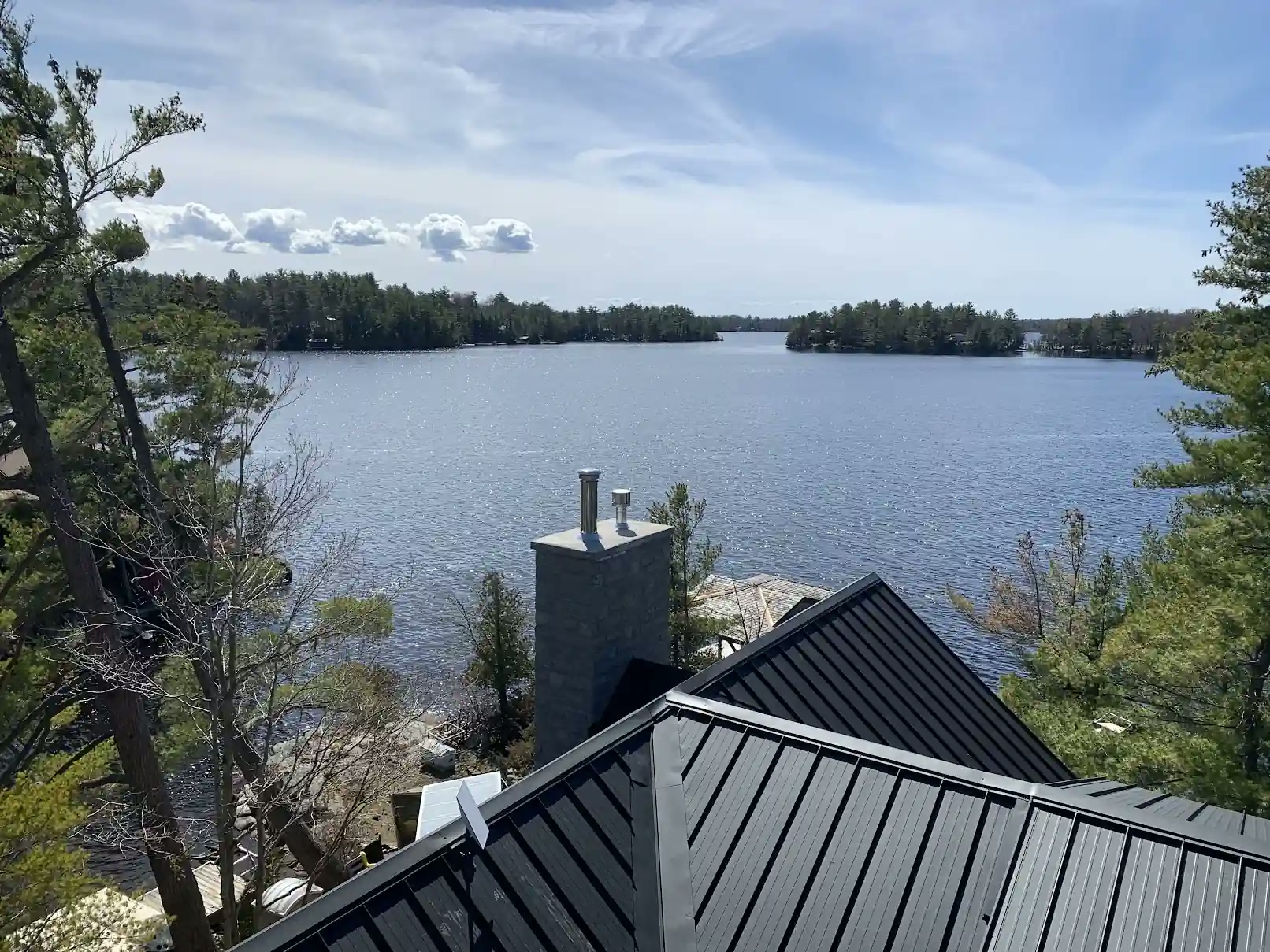 Dark standing seam metal roof and stone chimney on a waterfront cottage overlooking a treed Georgian Bay shoreline