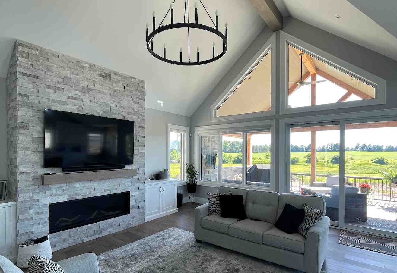 Cottage great room with a stone fireplace wall, vaulted timber ceiling, and a wall of windows overlooking open countryside